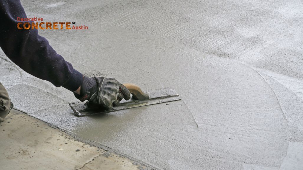 A person wearing gloves uses a trowel to smooth wet concrete on a surface, displaying a focus on craftsmanship.