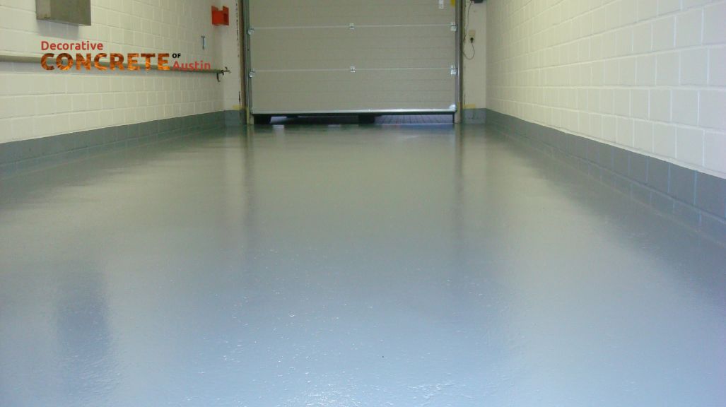 Smooth, glossy gray concrete floor of a garage, with white brick walls and a closed overhead door
