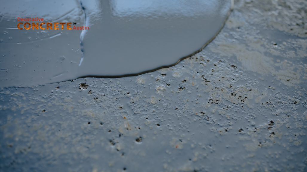 A close-up of wet concrete poured onto a textured surface, showing smooth liquid merging into rough texture.