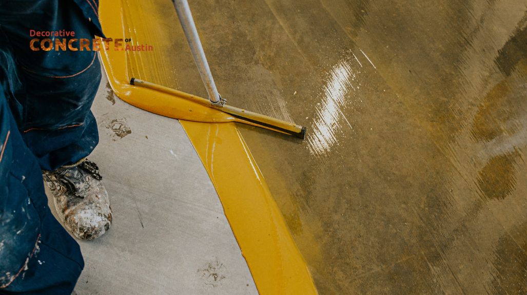 A worker in paint-splattered boots is smoothing a bright yellow coating over a concrete surface with a tool, conveying a sense of precision and craftsmanship
