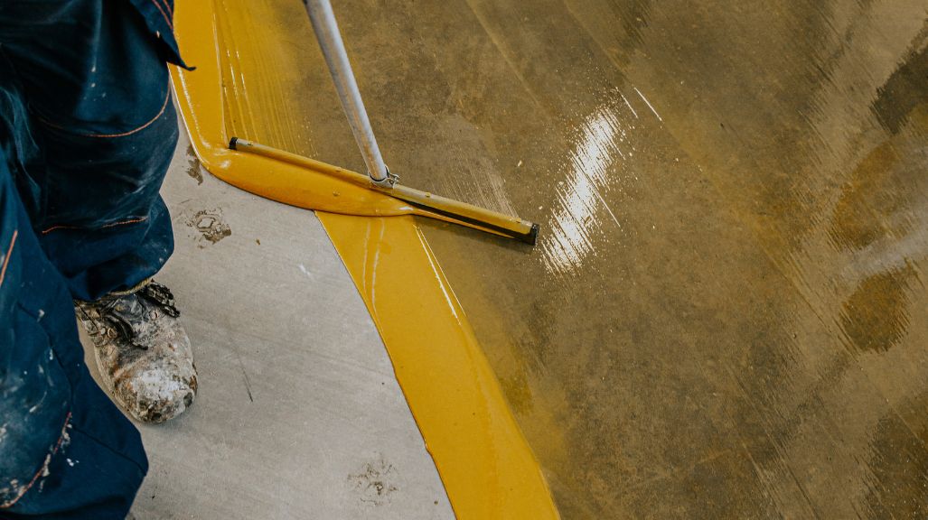 Close-up of a worker spreading glossy yellow epoxy on a concrete floor with a squeegee
