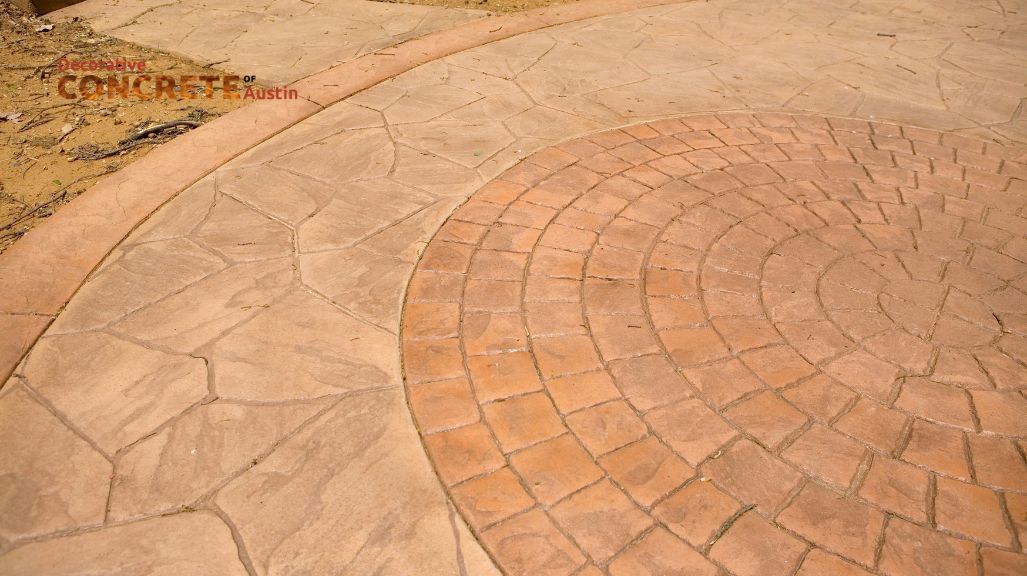 Circular, stamped concrete patio displaying a mix of earthy tones, featuring a central brick pattern surrounded by irregular stone-like shapes.