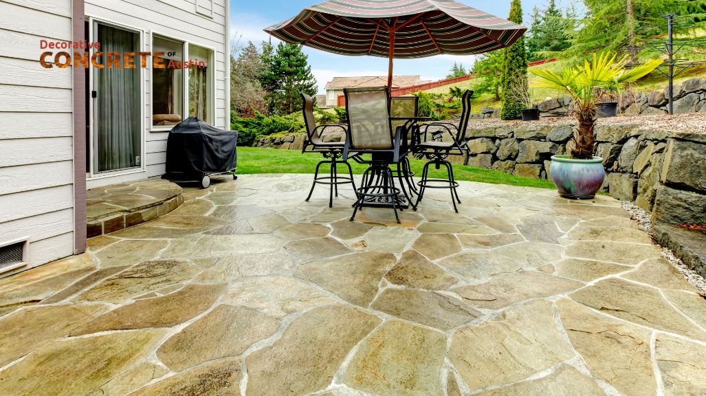 Stone patio with furniture and large umbrella, surrounded by a stone wall and lush garden