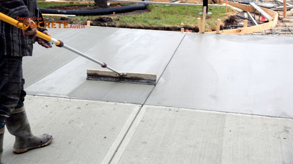 A worker smooths wet concrete on a sidewalk with a long tool.
