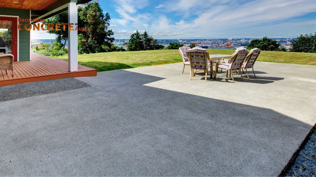 Spacious concrete patio with six cushioned chairs around a table, overlooking a lush lawn and scenic city view under a partly cloudy sky