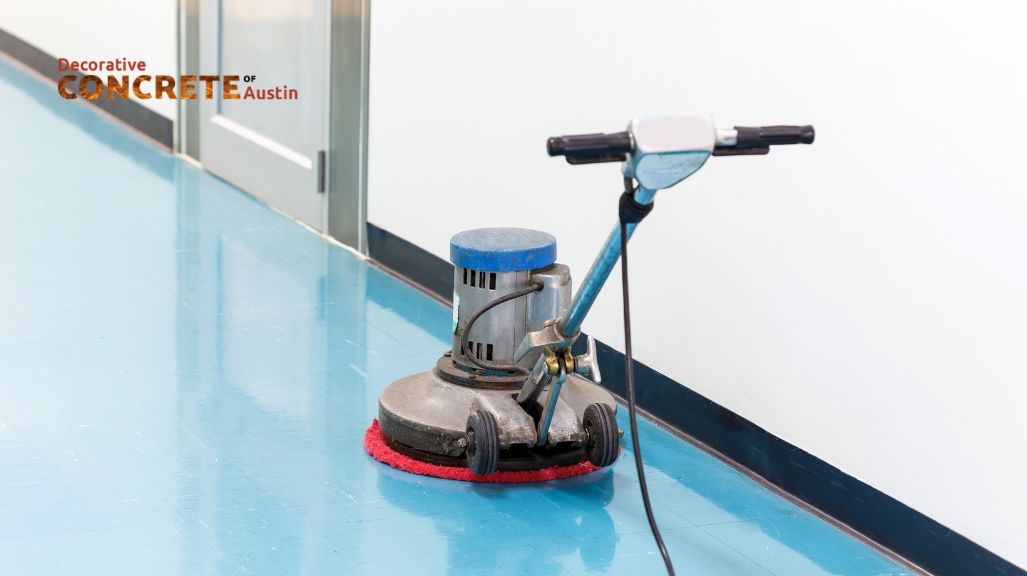 A floor polishing machine with a red pad rests on a shiny blue concrete floor. The scene conveys cleanliness and maintenance.