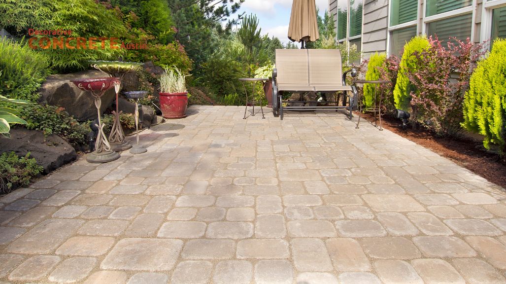 A stone-tiled patio with a table and chairs under an umbrella.