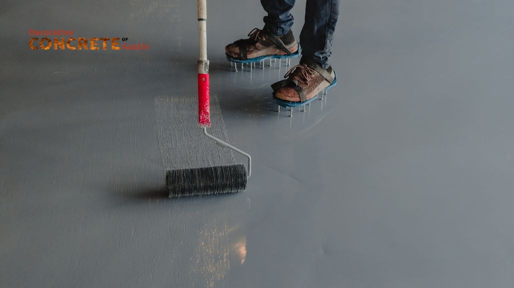 A person in spiked shoes uses a long-handled roller to apply a smooth gray finish on a concrete floor, conveying precision and professionalism.
