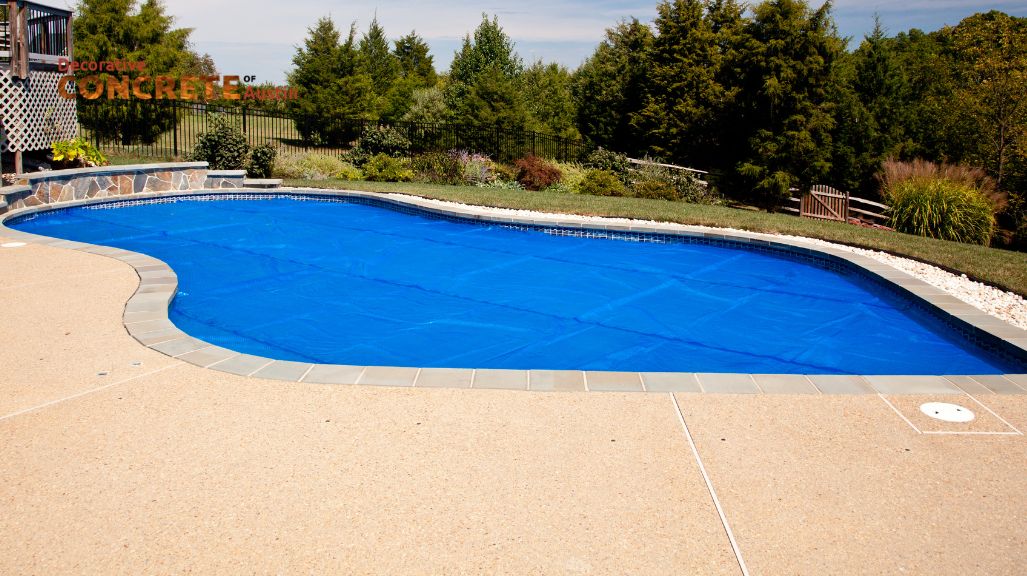 Backyard pool with a bright blue cover, surrounded by light-colored concrete.