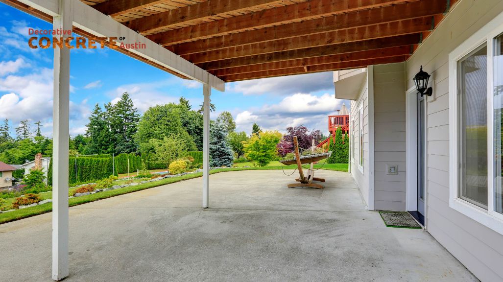 A spacious, concrete patio under a wooden pergola overlooks a vibrant garden with lush trees and plants