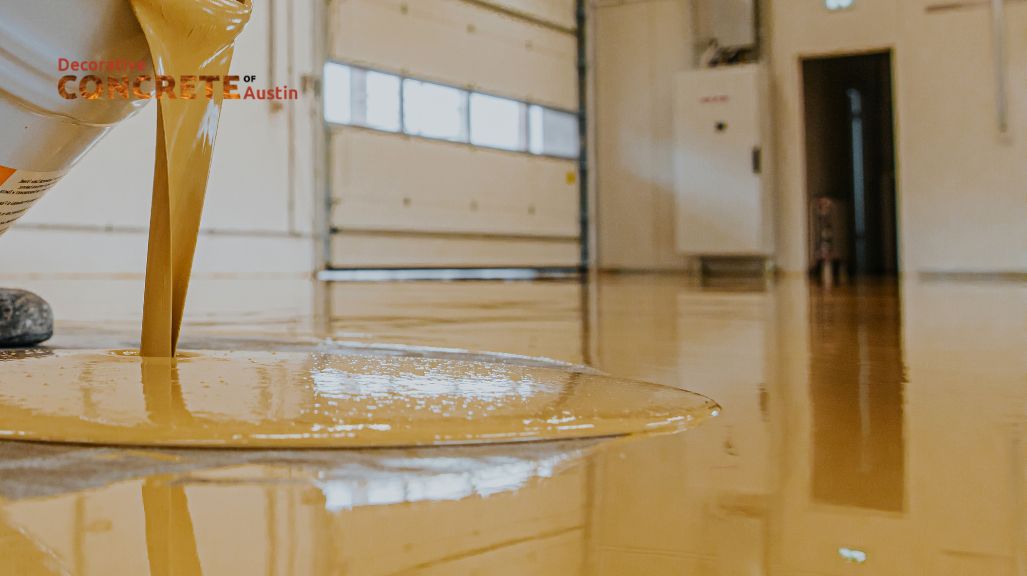 A close-up of golden-brown liquid being poured onto a smooth garage floor, creating a glossy finish.