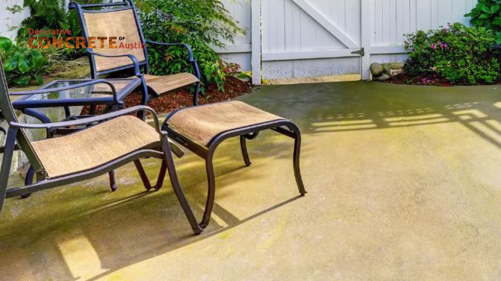 A sunny patio with two metal-framed chairs and a matching footrest on a smooth concrete floor.