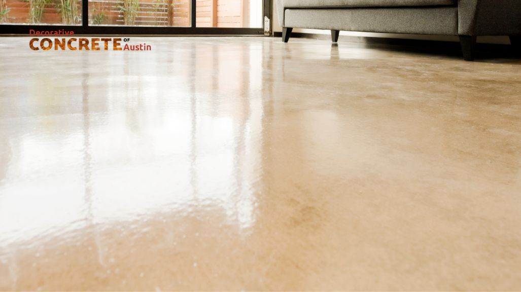 A polished concrete floor reflects light, creating a smooth, glossy surface in a modern room with a gray sofa and large glass doors, conveying elegance.