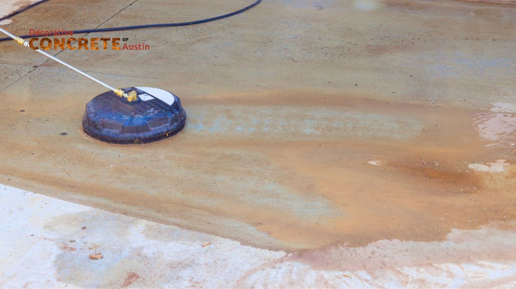 A power washer cleans a stained concrete surface, revealing a lighter, cleaner area.
