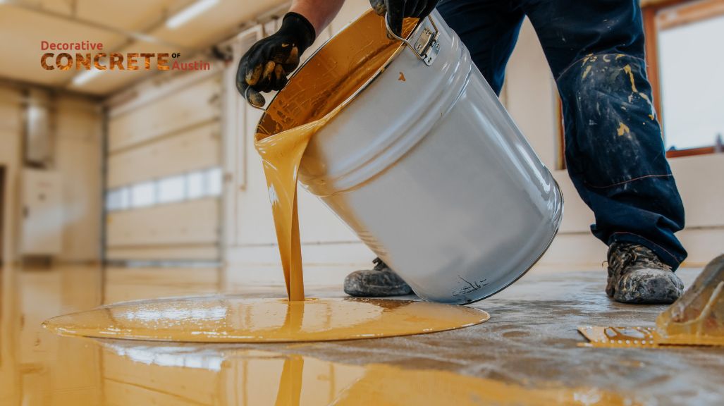 A person pours golden epoxy onto a garage floor from a metal bucket, wearing work gloves and jeans, creating a smooth, glossy surface with precision