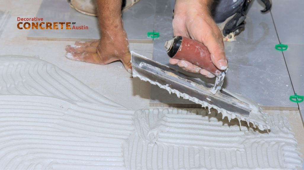 A worker smooths tile adhesive on a floor with a trowel, preparing for tile placement. 
