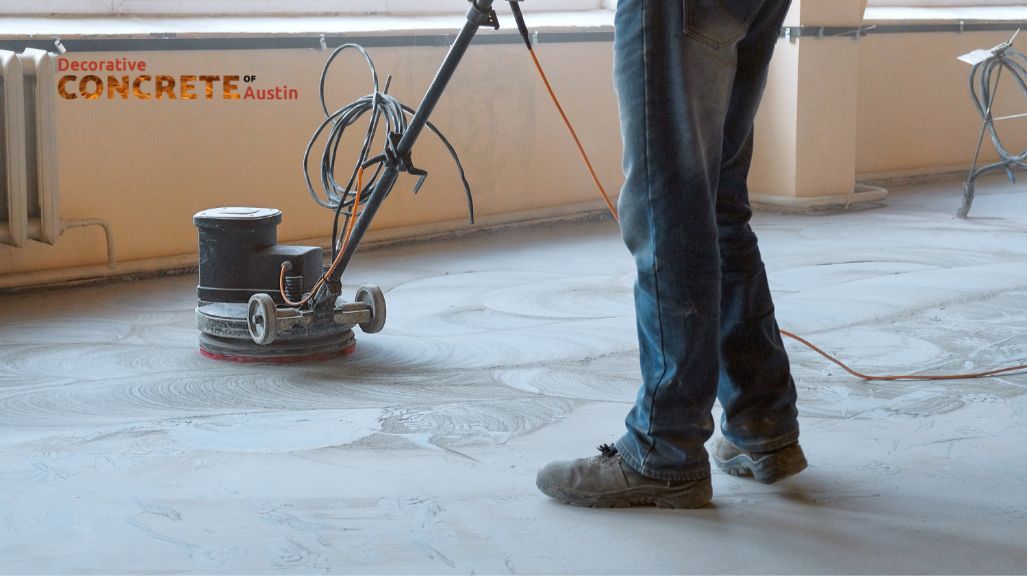 A worker in jeans and boots operates a floor polishing machine on a concrete surface