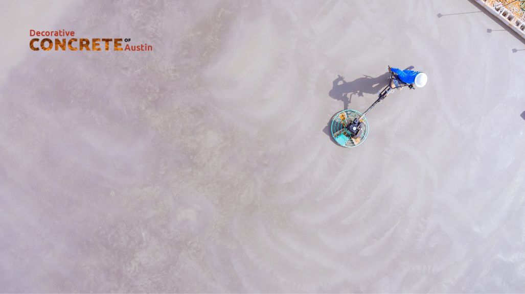 Aerial view of a concrete surface being polished by machinery operated by a worker in blue. 