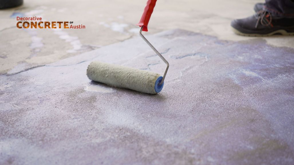 A paint roller with a red handle applies a layer of finish on a concrete surface