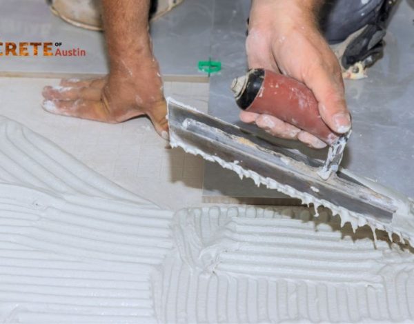 A worker smooths tile adhesive on a floor with a trowel, preparing for tile placement.